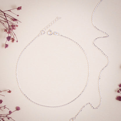 Silver anklet on a light pink background with dried flowers